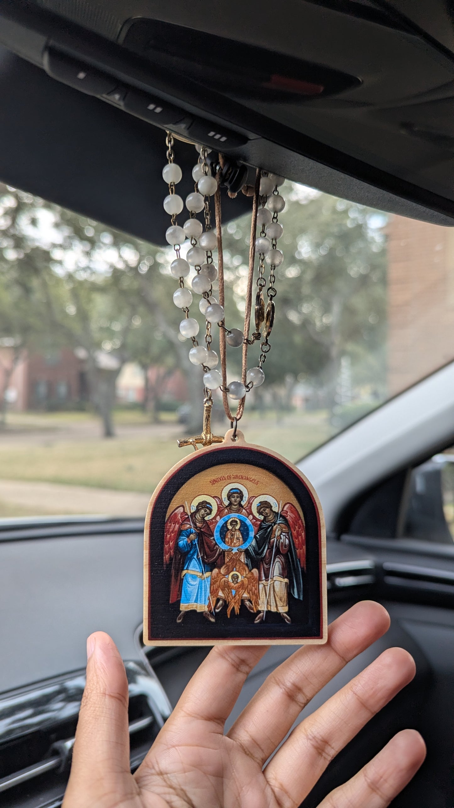 Hand holding a religious icon with rosary in a car